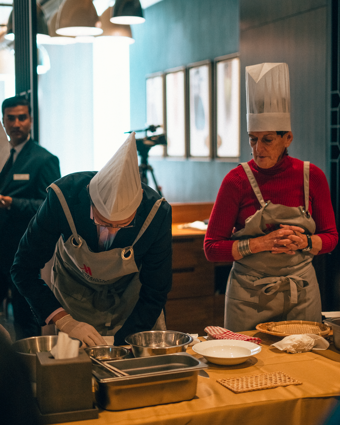 services-01 Two chefs in aprons and hats working in a professional kitchen setting.