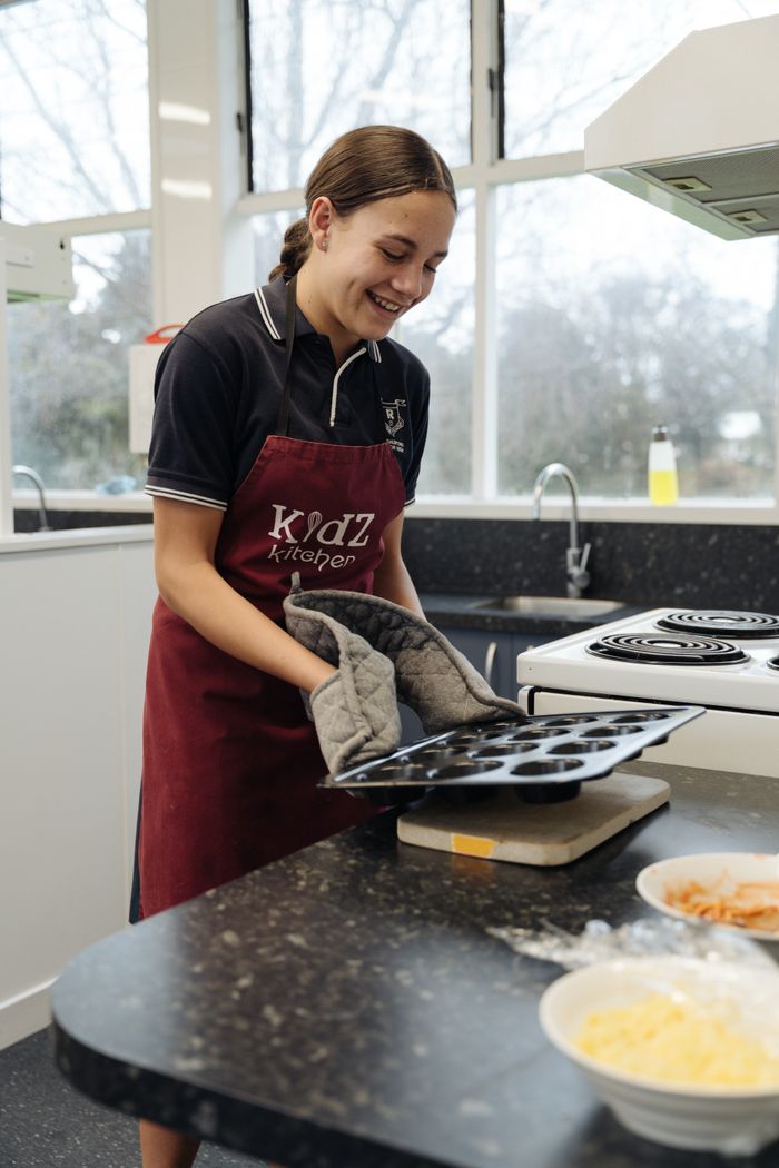 services-01 Smiling young woman in an apron baking muffins in a modern kitchen.