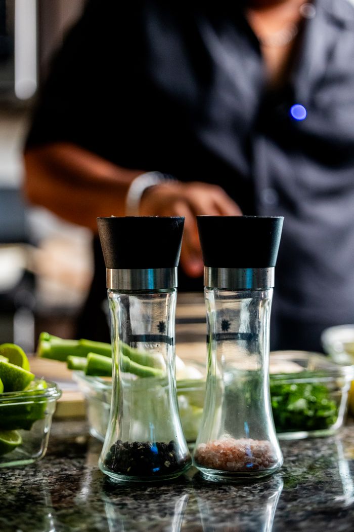 services-01 Salt and pepper grinders on kitchen counter with chef cooking in the background.