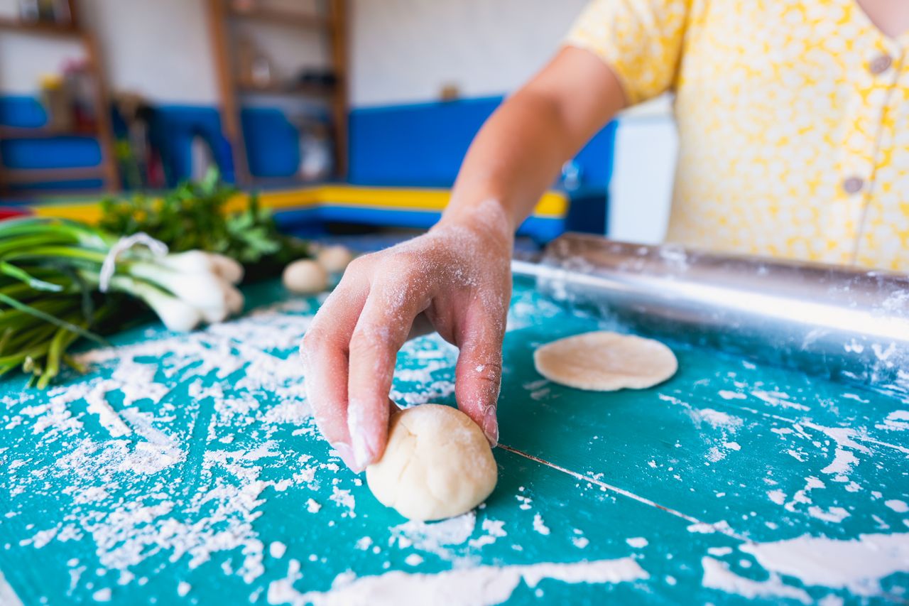 A person preparing dough by hand in a colorful kitchen setting. Ideal for cooking or baking themes.