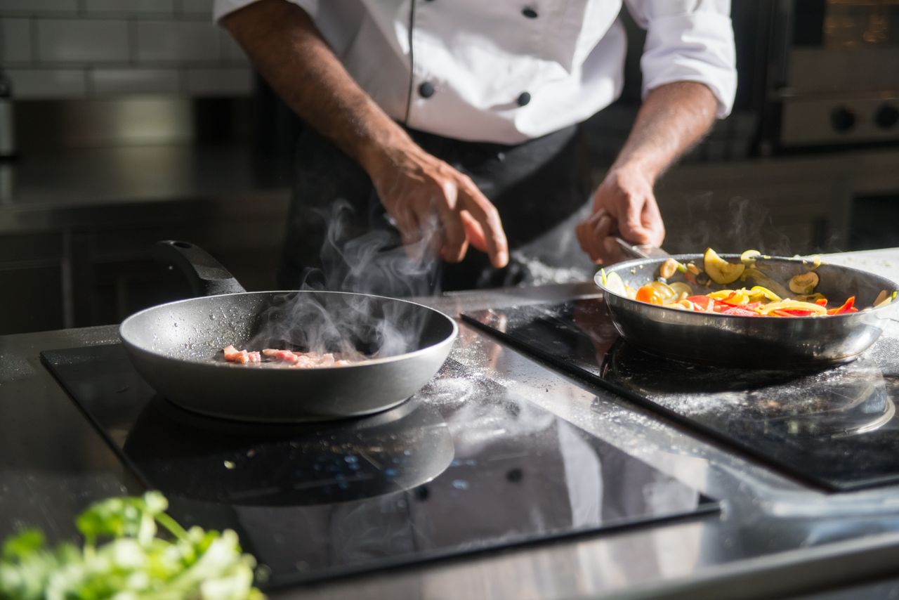 vision A chef skillfully prepares a meal with fresh ingredients on an electric stove, emphasizing culinary expertise.